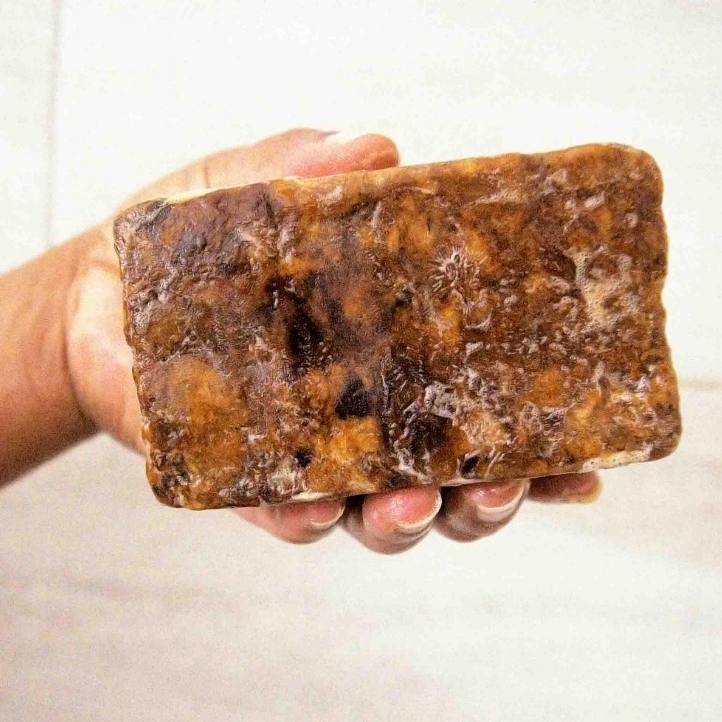 Hand holding a marbled brown and tan bar of artisan soap with rich lather, perfect for natural skincare routines.