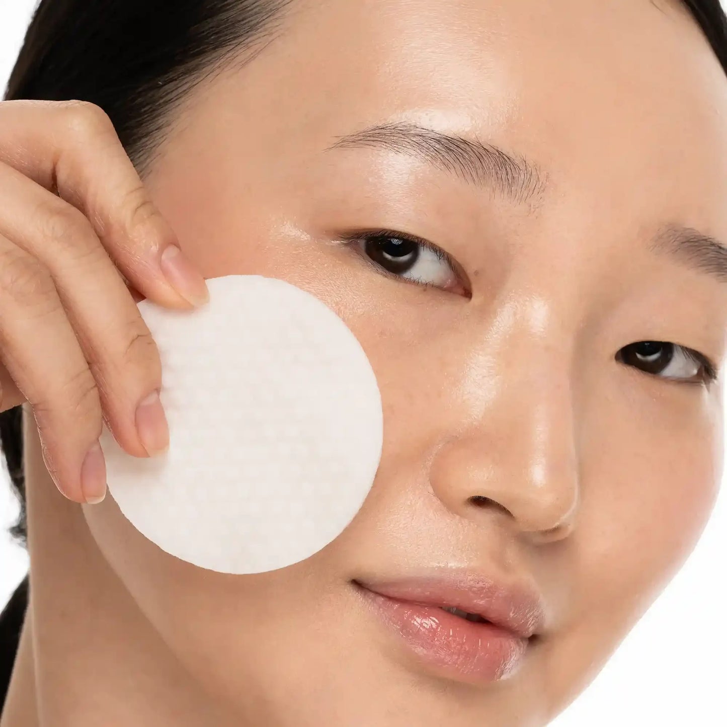 Woman applying cotton pad to glowing skin for skincare routine
