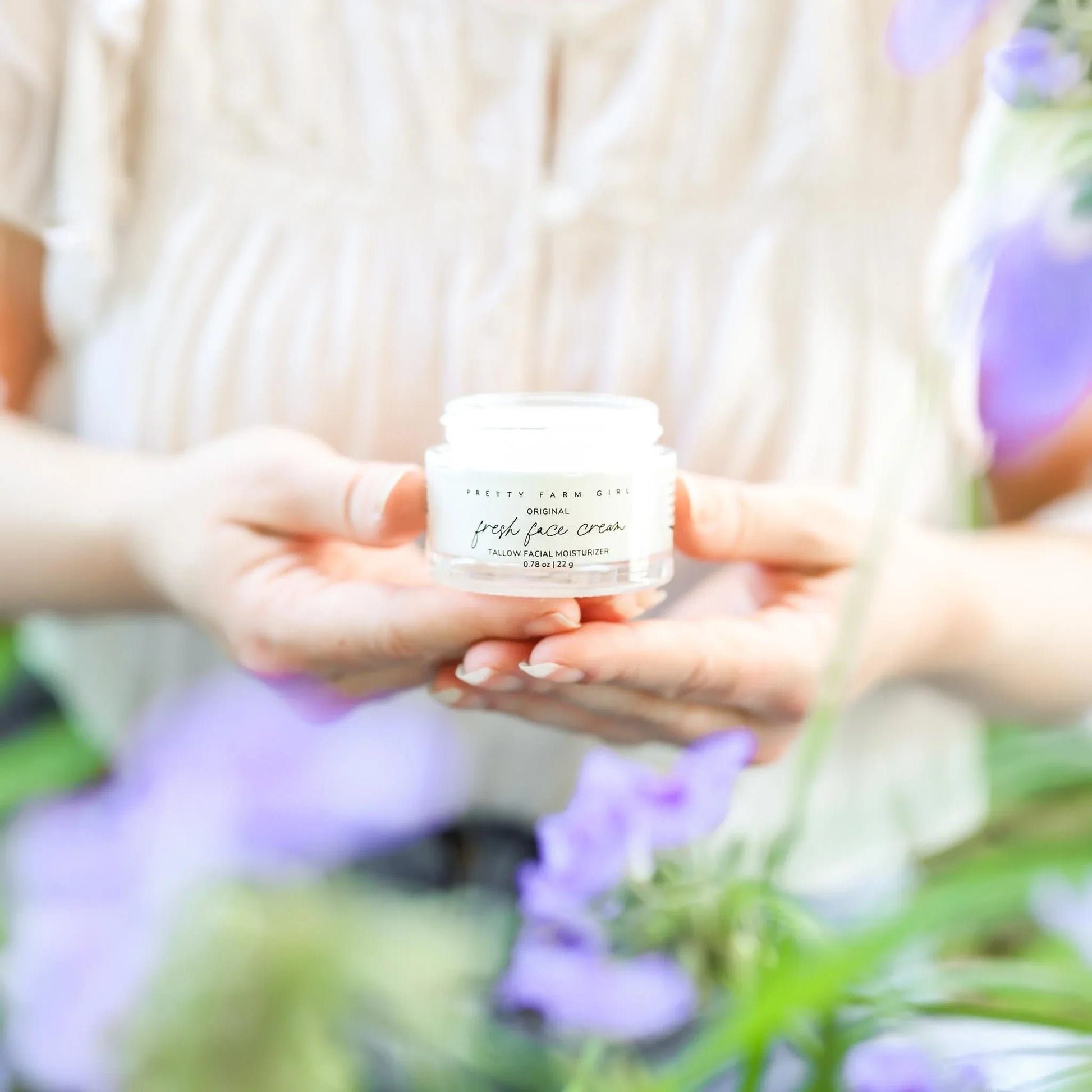 Fresh face cream in hands with purple flowers, natural skincare product
