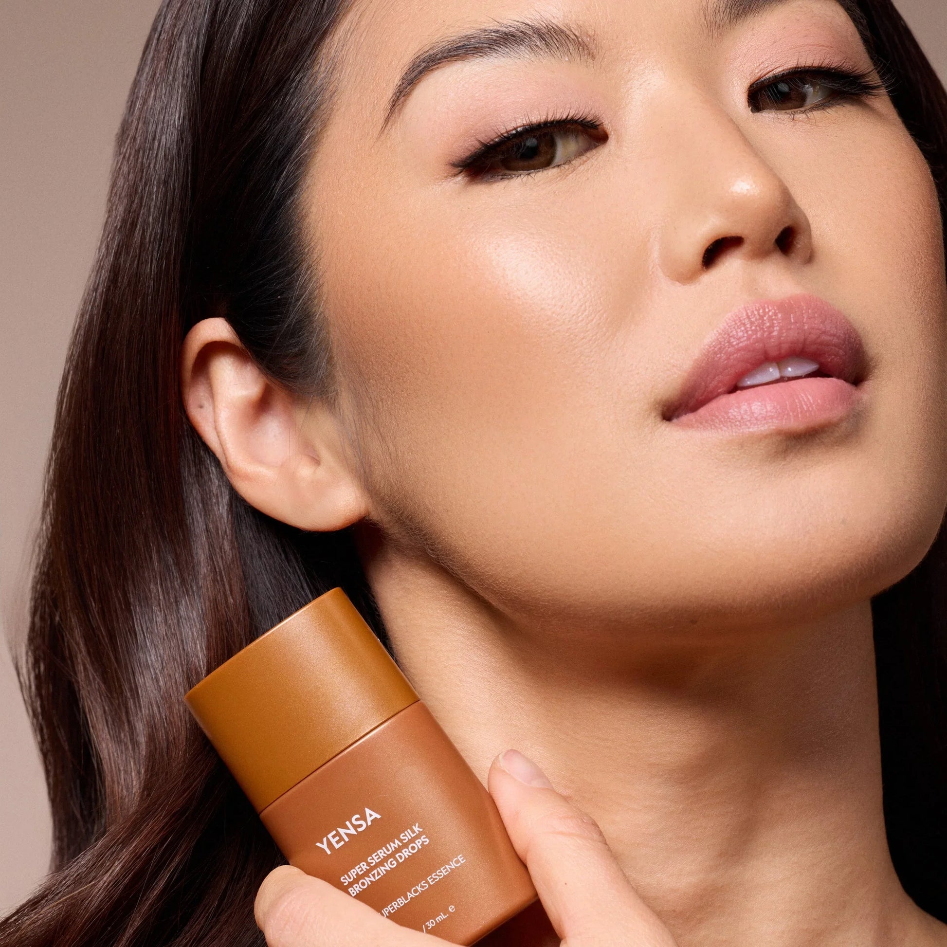 YENSA Super Serum Silk Bronzing Drops for radiant glow, held near model's glowing skin